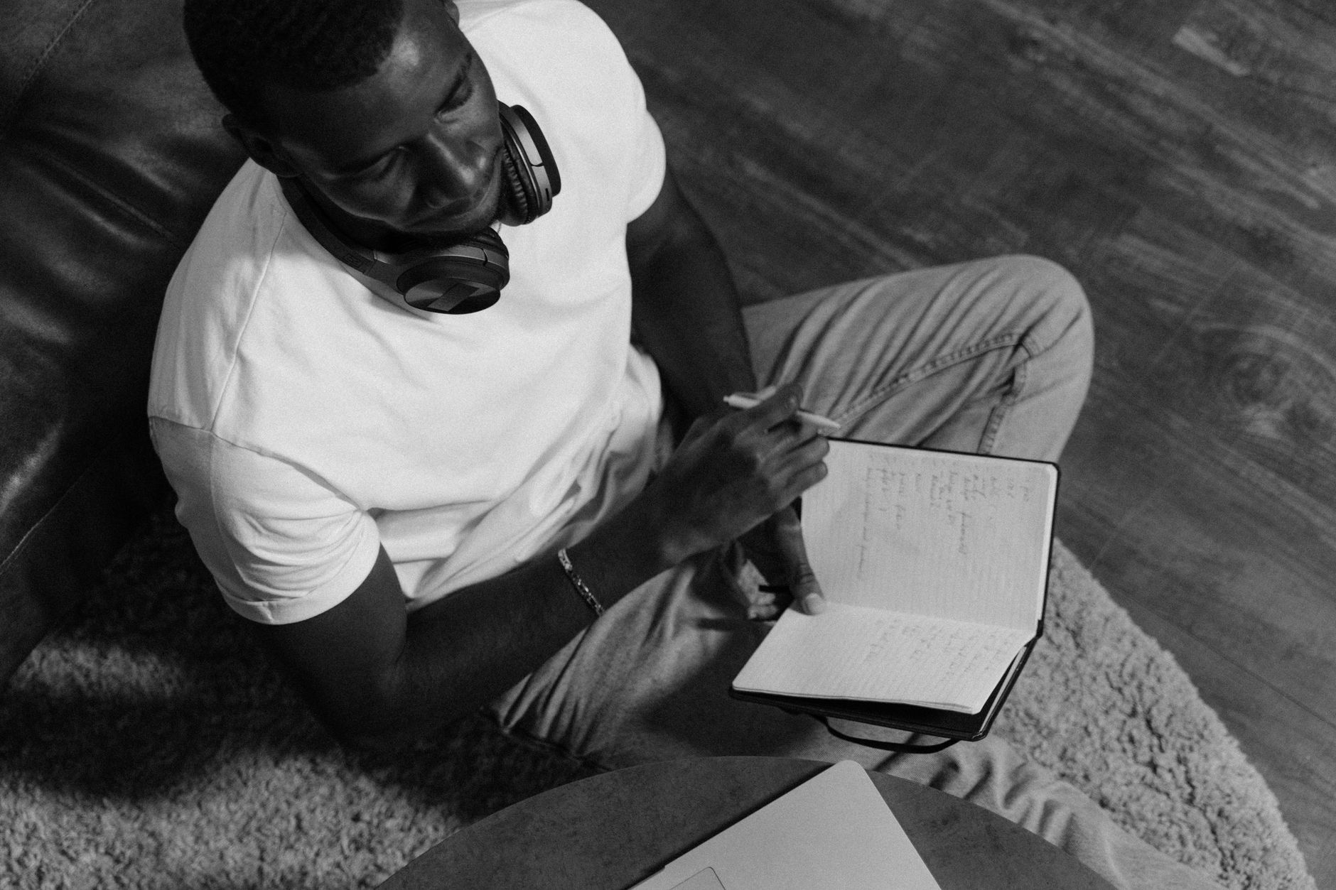 Un hombre con auriculares al cuello sostiene un cuaderno abierto y un bolígrafo junto a un portátil, en una imagen en blanco y negro